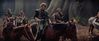 Movie still from “Krull” (1983), directed by Peter Yates – Two men on horseback in the woods with trees in the background; Medium shot, Low angle