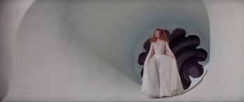 Movie still from “Krull” (1983), directed by Peter Yates – A woman in a white dress standing next to a wall; Wide shot, Low angle