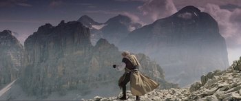 Movie still from “Krull” (1983), directed by Peter Yates – A man standing on top of a mountain holding a gun; Wide shot, Low angle