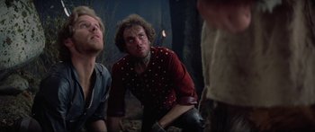 Movie still from “Krull” (1983), directed by Peter Yates – A man in a red shirt is sitting next to another man in a red shirt; Medium shot, Low angle