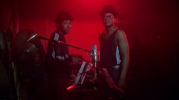 Movie still from “Krush Groove” (1985), directed by Michael Schultz – A couple of men standing next to each other in front of a microphone; Medium shot, Low angle