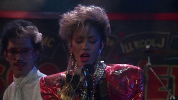 Movie still from “Krush Groove” (1985), directed by Michael Schultz – A woman in a red jacket singing into a microphone; Close Up shot, Over the shoulder angle