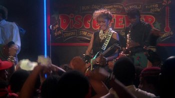 Movie still from “Krush Groove” (1985), directed by Michael Schultz – A woman is playing guitar in front of a group of people; Medium shot, Over the shoulder angle