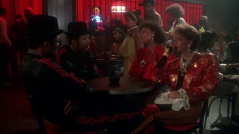 Movie still from “Krush Groove” (1985), directed by Michael Schultz – A group of people sitting at a table with drinks; Medium shot, Over the shoulder angle