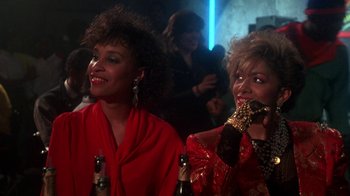 Movie still from “Krush Groove” (1985), directed by Michael Schultz – A couple of women standing next to each other in a room; Medium shot, Over the shoulder angle