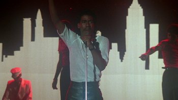 Movie still from “Krush Groove” (1985), directed by Michael Schultz – A man in a white shirt is holding a microphone; Medium shot, Low angle
