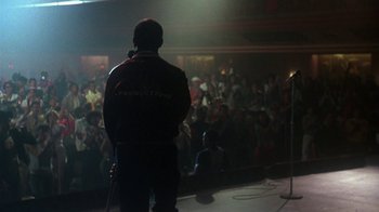 Movie still from “Krush Groove” (1985), directed by Michael Schultz – A man standing in front of an audience on a stage; Wide shot, Over the shoulder angle