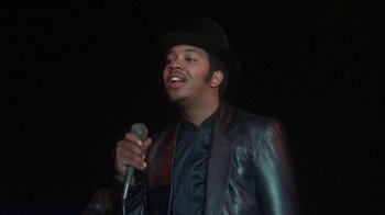 Movie still from “Krush Groove” (1985), directed by Michael Schultz – A man wearing a hat and a leather jacket holding a microphone; Close Up shot, Low angle