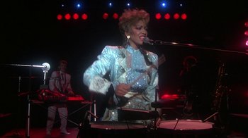 Movie still from “Krush Groove” (1985), directed by Michael Schultz – A woman in a blue and white jacket singing; Medium shot, Low angle