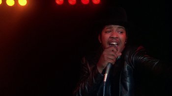 Movie still from “Krush Groove” (1985), directed by Michael Schultz – A man in a black hat is singing into a microphone; Close Up shot, Low angle