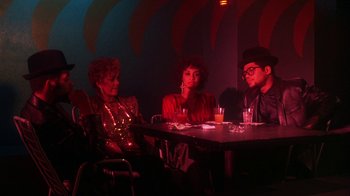 Movie still from “Krush Groove” (1985), directed by Michael Schultz – A group of people sitting at a table in a room; Medium shot, Low angle