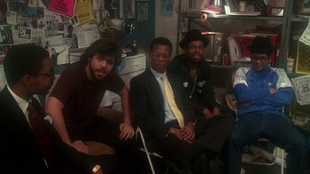 Movie still from “Krush Groove” (1985), directed by Michael Schultz – A group of men sitting next to each other in a room; Medium shot, High angle