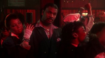 Movie still from “Krush Groove” (1985), directed by Michael Schultz – A man in a suit and tie holding a cell phone in his hand; Close Up shot, Low angle