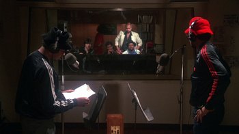 Movie still from “Krush Groove” (1985), directed by Michael Schultz – A man reading a paper in front of a microphone; Medium shot, Over the shoulder angle