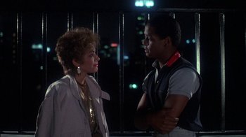 Movie still from “Krush Groove” (1985), directed by Michael Schultz – A man and a woman standing next to each other in front of a window; Medium shot, Over the shoulder angle