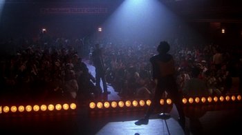 Movie still from “Krush Groove” (1985), directed by Michael Schultz – A group of people standing in front of an audience on a stage; Wide shot, Low angle