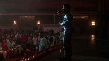 Movie still from “Krush Groove” (1985), directed by Michael Schultz – A man is speaking into a microphone in front of an audience; Wide shot, Low angle