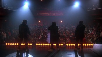 Movie still from “Krush Groove” (1985), directed by Michael Schultz – A group of people standing on a stage in front of an audience; Wide shot, Low angle