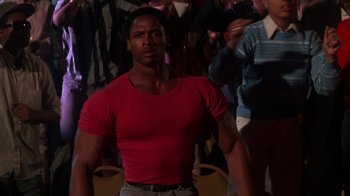 Movie still from “Krush Groove” (1985), directed by Michael Schultz – A man in a red t - shirt is standing in front of a crowd; Medium shot, Low angle