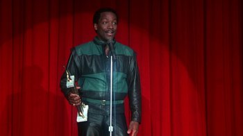 Movie still from “Krush Groove” (1985), directed by Michael Schultz – A man holding an award while standing on a stage; Medium shot, Low angle
