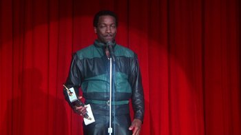 Movie still from “Krush Groove” (1985), directed by Michael Schultz – A man standing on a stage holding a microphone; Medium shot, Low angle