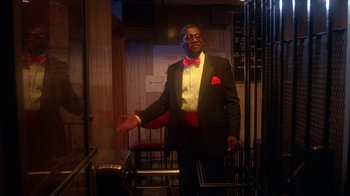 Movie still from “Krush Groove” (1985), directed by Michael Schultz – A man in a suit and bow tie standing in front of a chair; Medium shot, Low angle