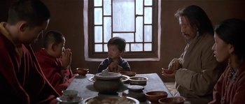 Movie still from “Kundun” (1997), directed by Martin Scorsese – A young child sitting at a table with a bowl of food; Medium shot, Over the shoulder angle