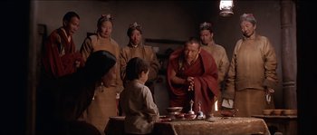 Movie still from “Kundun” (1997), directed by Martin Scorsese – A group of people standing around a table with food on top of it; Medium shot, High angle