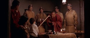Movie still from “Kundun” (1997), directed by Martin Scorsese – A group of people standing around a table with food; Medium shot, High angle