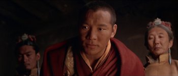 Movie still from “Kundun” (1997), directed by Martin Scorsese – A man in a red and yellow robe is posing for a picture; Close Up shot, High angle