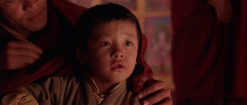 Movie still from “Kundun” (1997), directed by Martin Scorsese – A young boy wearing a monk's robe and holding his hand on his shoulder; Close Up shot, Over the shoulder angle