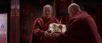 Movie still from “Kundun” (1997), directed by Martin Scorsese – Two men in robes are holding a suitcase; Medium shot, High angle