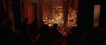 Movie still from “Kundun” (1997), directed by Martin Scorsese – People sitting in front of a large buddha statue; Wide shot, Low angle