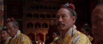 Movie still from “Kundun” (1997), directed by Martin Scorsese – A man with a mustache and a flower in his hair; Close Up shot, Low angle