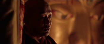 Movie still from “Kundun” (1997), directed by Martin Scorsese – A man in a red and white robe looking at the camera; Close Up shot, Low angle