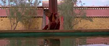 Movie still from “Kundun” (1997), directed by Martin Scorsese – A young child is playing with a stick in the water; Wide shot, High angle