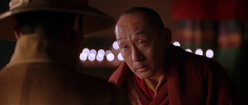 Movie still from “Kundun” (1997), directed by Martin Scorsese – An older man wearing a red and yellow robe; Close Up shot, Over the shoulder angle