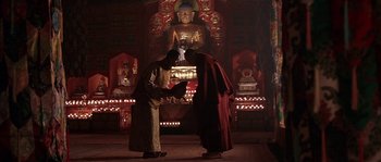 Movie still from “Kundun” (1997), directed by Martin Scorsese – Two men in traditional garb in front of a statue of buddha; Wide shot, Low angle