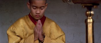 Movie still from “Kundun” (1997), directed by Martin Scorsese – A young boy in a yellow and red outfit is praying; Close Up shot, High angle