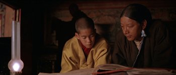 Movie still from “Kundun” (1997), directed by Martin Scorsese – A young man sitting in front of an open book; Medium shot, High angle