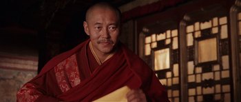 Movie still from “Kundun” (1997), directed by Martin Scorsese – A man in a red and yellow robe is holding a sheet of paper; Close Up shot, Low angle