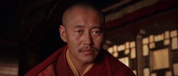 Movie still from “Kundun” (1997), directed by Martin Scorsese – A man with a shaved head wearing a red and yellow robe; Close Up shot, Low angle