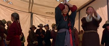 Movie still from “Kundun” (1997), directed by Martin Scorsese – A woman in traditional clothing is praying in front of a group of people; Medium shot, Low angle