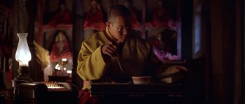 Movie still from “Kundun” (1997), directed by Martin Scorsese – A man in a yellow jacket is eating food; Medium shot, High angle