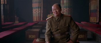 Movie still from “Kundun” (1997), directed by Martin Scorsese – An older man in a military uniform sitting on a chair; Medium shot, Low angle