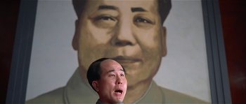 Movie still from “Kundun” (1997), directed by Martin Scorsese – A man with a surprised look standing in front of a painting of mao zedong; Close Up shot, Low angle