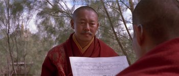 Movie still from “Kundun” (1997), directed by Martin Scorsese – A man in a red and yellow robe holding a document; Close Up shot, Over the shoulder angle