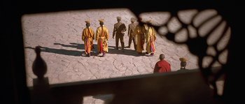 Movie still from “Kundun” (1997), directed by Martin Scorsese – A group of men standing on top of a dirt field; Extreme Wide shot, High angle