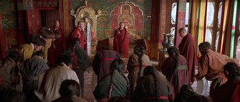 Movie still from “Kundun” (1997), directed by Martin Scorsese – A group of people sitting in front of a painting of a buddha; Wide shot, High angle