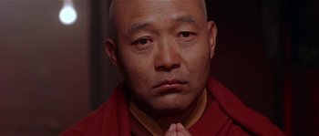Movie still from “Kundun” (1997), directed by Martin Scorsese – A man in a red robe is praying; Close Up shot, Low angle